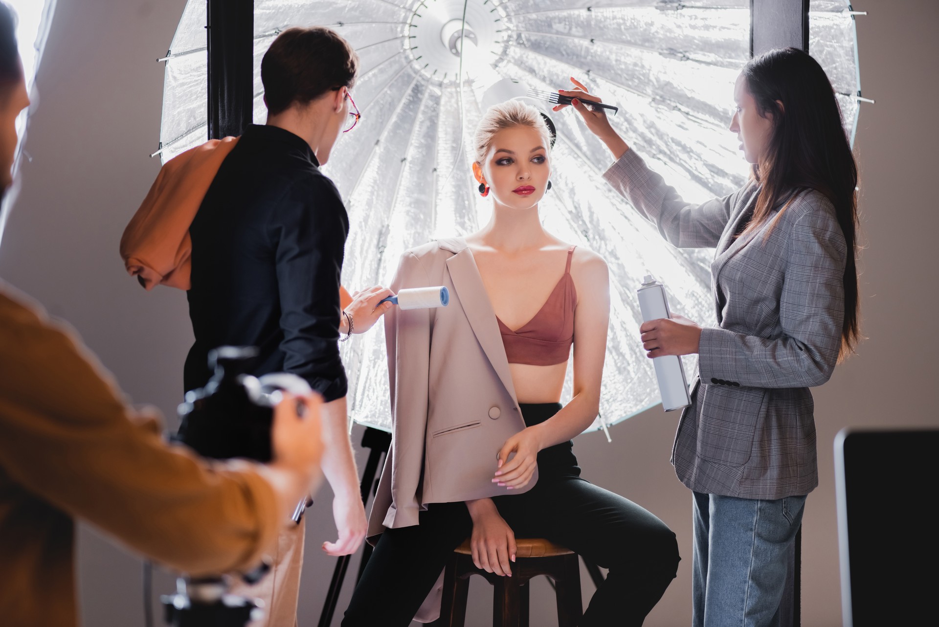 selective focus of stylist using lint roller and hairstylist doing hairstyle to stylish model on backstage